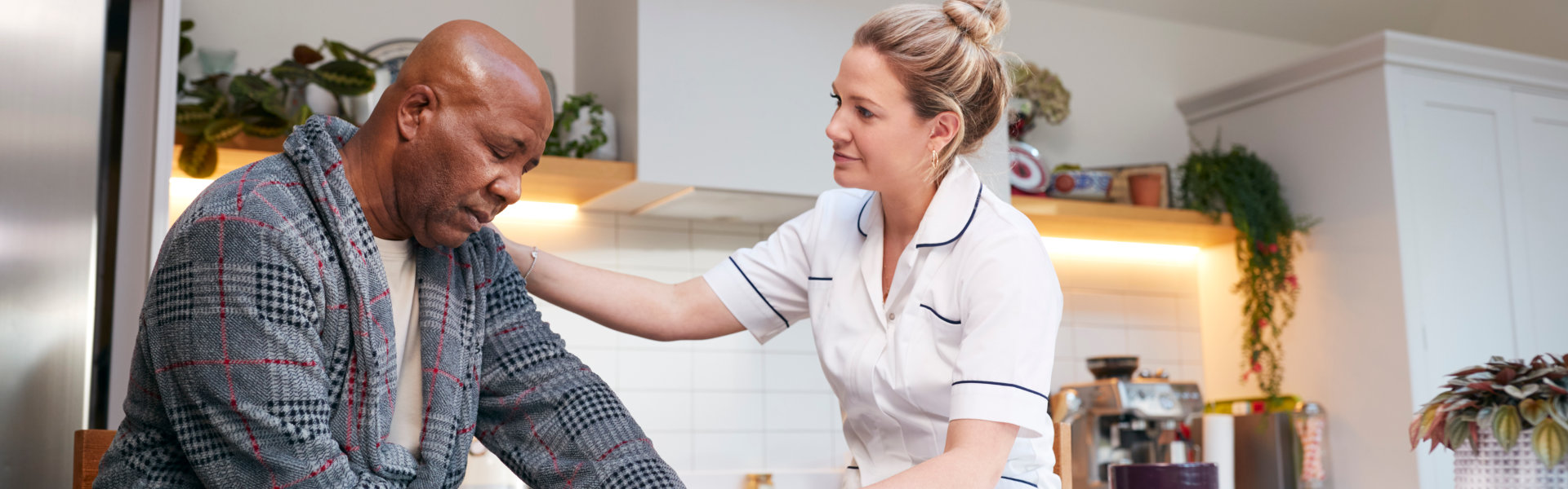 Mature Man In Dressing Gown Talking With Female Nurse In Kitchen At Home